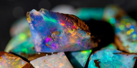A photo of an opal with pink, blue, orange and green colouring sitting on top of an out of focus pile of green opals