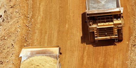 Aerial shot of two dump trucks approaching each other on a dirt road.