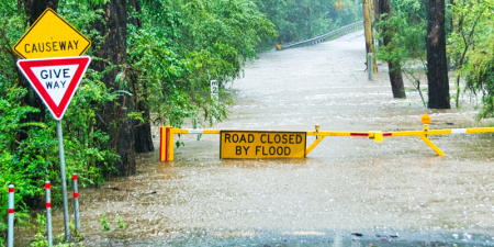 a give way sign in front of a flooded road, which has a barrier and a sign that says "Road closed by flood".